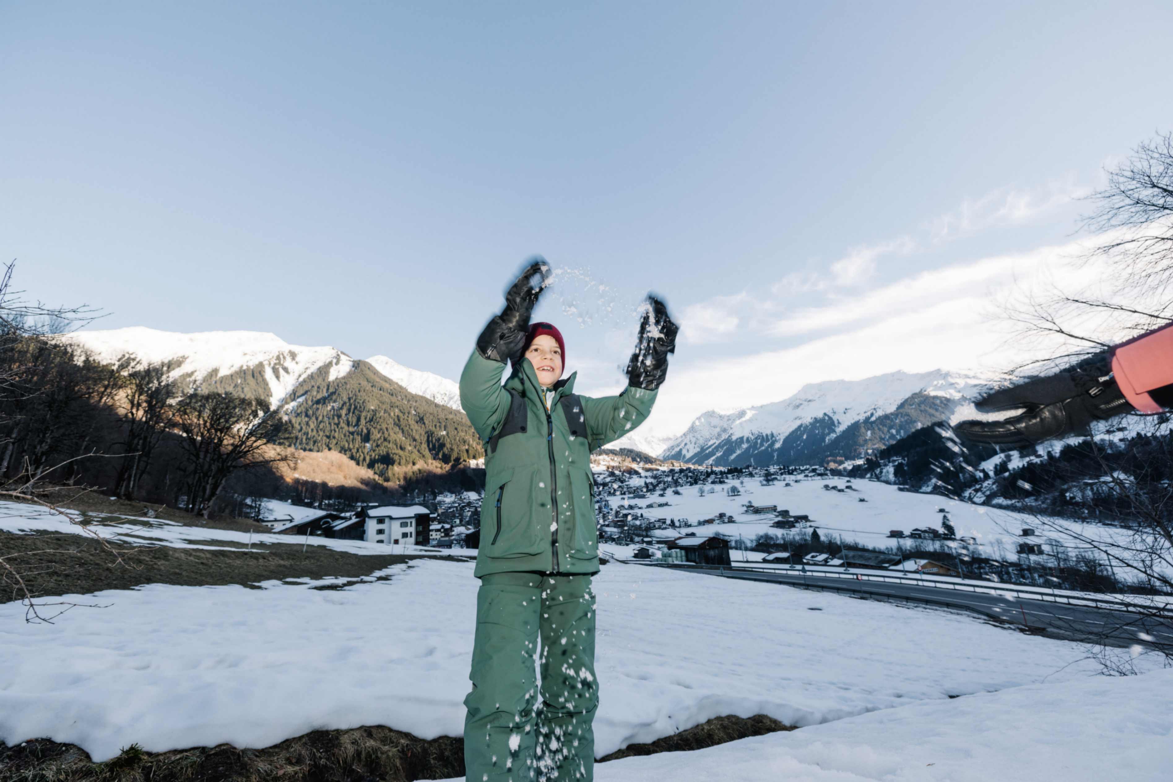 Ein Junge mit Belowzero Bekleidung wirft Schnee in die Höhe