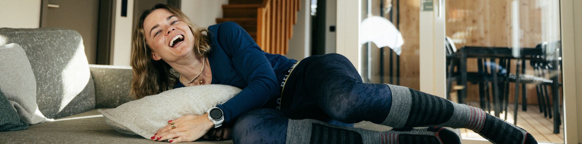 EIne Dame sitzt in Belowzero Bekleidung auf dem Sofa und liesst ein Buch.
