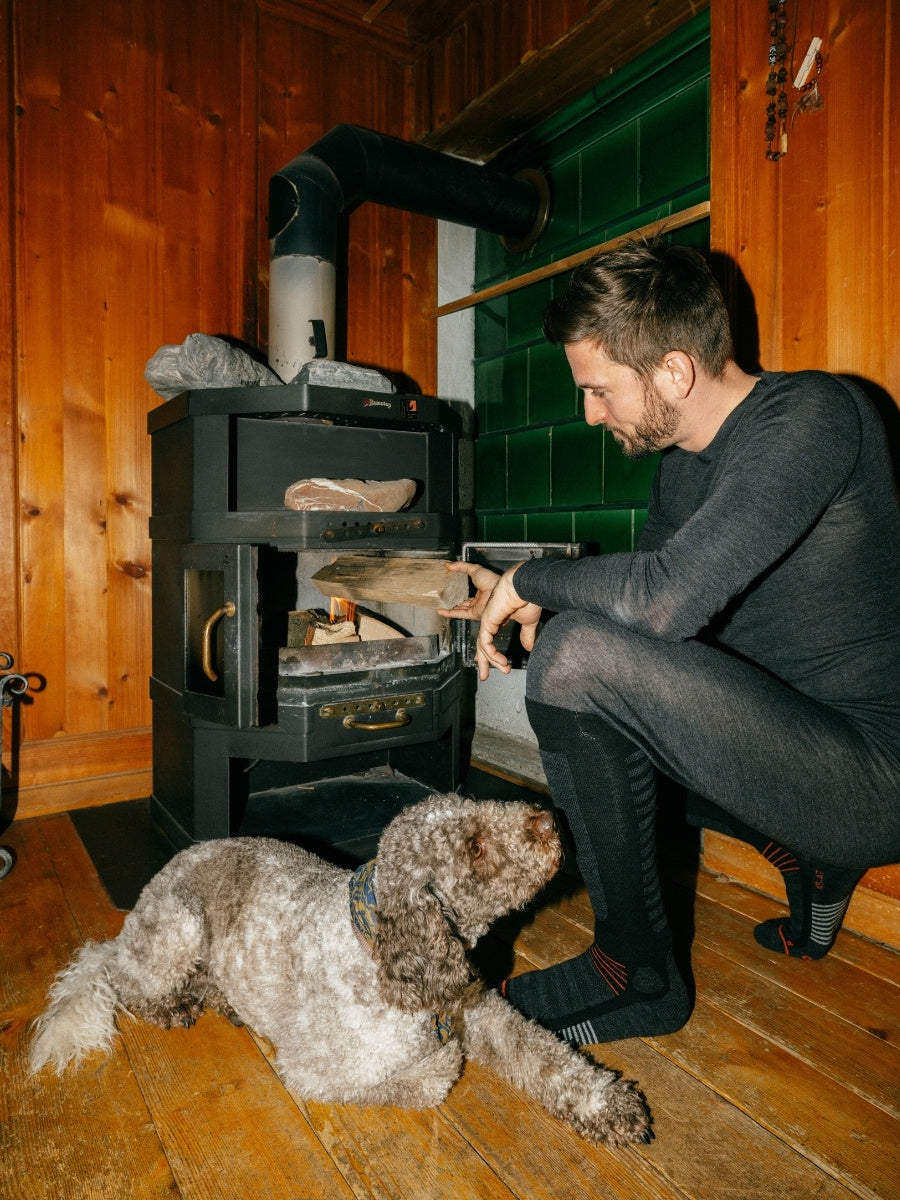 Ein Herr macht mit dem Merino Belwozero Baselayer Outfit ein Feuer in der Stube.