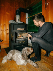 Ein Herr macht mit dem Merino Belwozero Baselayer Outfit ein Feuer in der Stube.