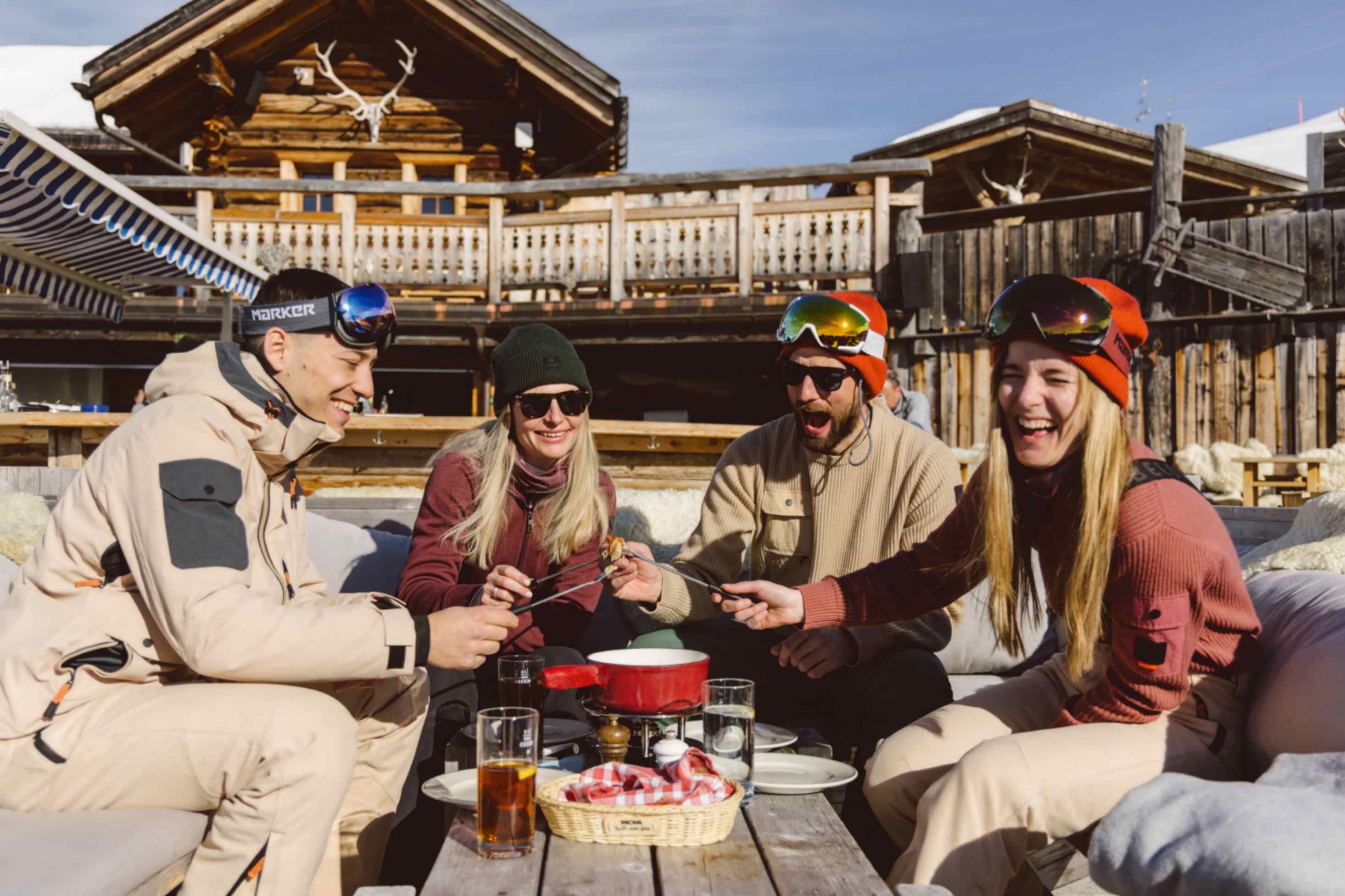 Eine Gruppe die auf einer Berghütte ein Fondue zusammen geniesst, dabei tragen alle Skibekleidung von Belowzero.