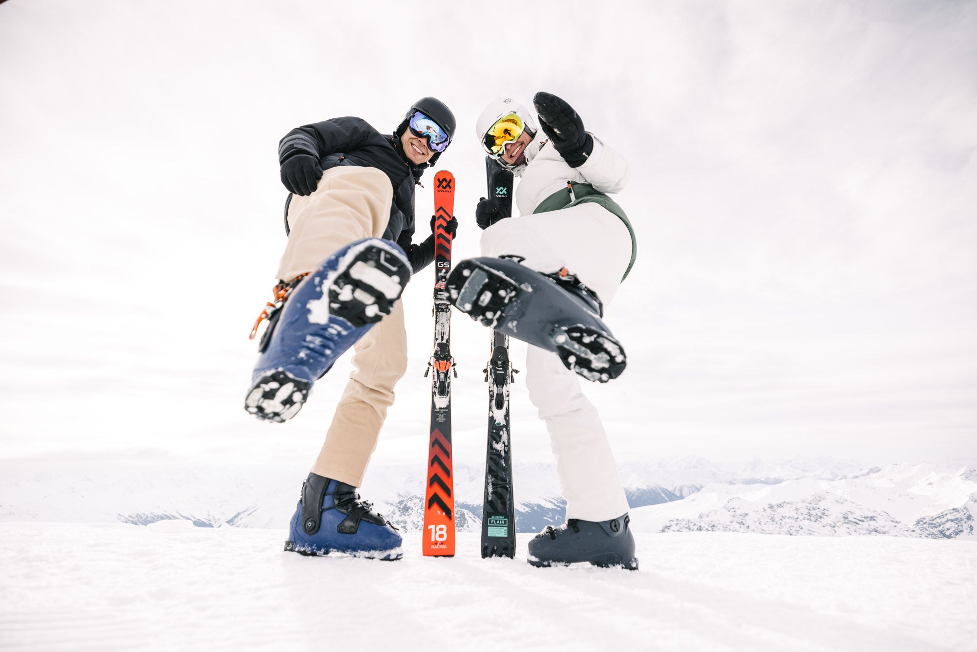 Eine Dame und ein Herr in Belowzero Bekleidung stehen auf der Piste mit gesamter Skiausrüstung.