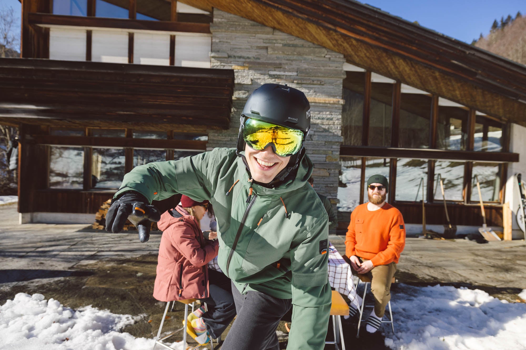 Skifahrer welcher vor einem Chalet steht und in die Kamera schaut.