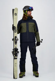 Ein Herrenmodel trägt die Leysin Jacke / Skijacke von Belowzero in navy/grün. Auf dem Bild ist die Ganzkörperansicht zu sehen.