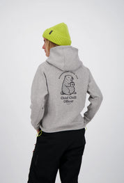 Rückenansicht einer Frau im grauen Belowzero Kapuzenpullover mit Murmeltier-Print "Chief Chill Officer", neongelber Beanie-Mütze und schwarzer Outdoorhose.