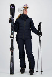 Frau in dunkelblauem Belowzero Skianzug mit Skijacke und Skihose, Völkl Skiern, Skistöcken sowie weissem Helm und Skibrille.