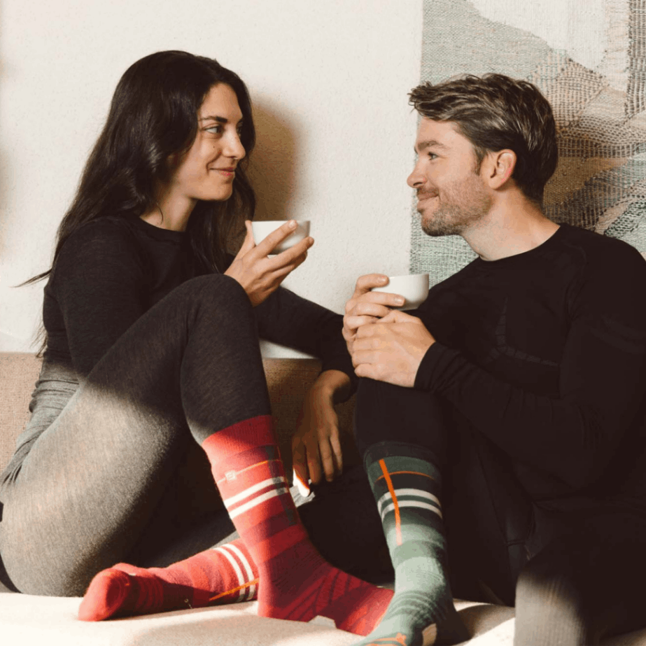 Eine Dame und ein Herr tragen Belowzero Baselayer Unterwäsche und sitzten auf einem Sofa