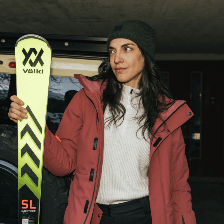 Eine Dame trägt ein Belowzero Skioutfit und hält Skier in den Händen