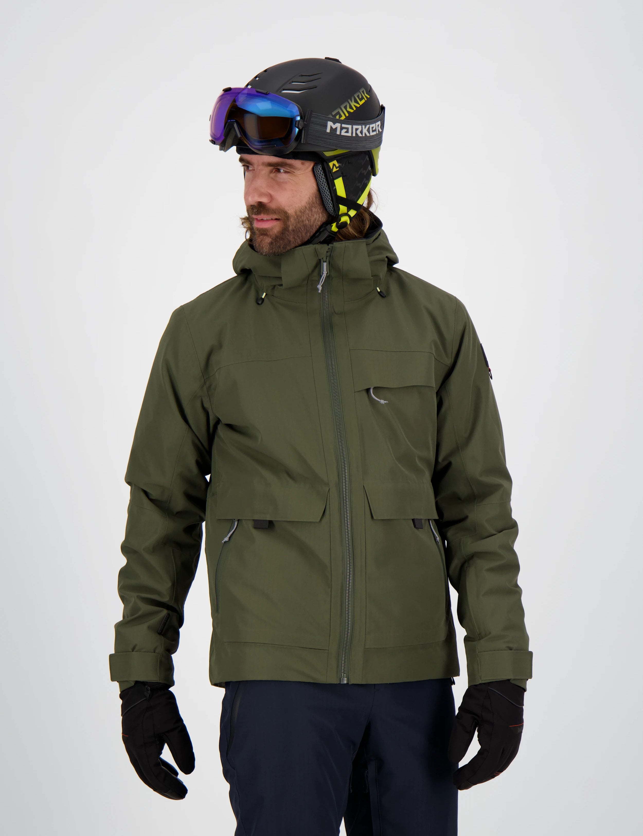 Mann trägt eine olivgrüne Belowzero Herren-Skijacke mit Kapuze und Taschen, dunkle Skihose, schwarze Handschuhe sowie einen Skihelm mit Skibrille.