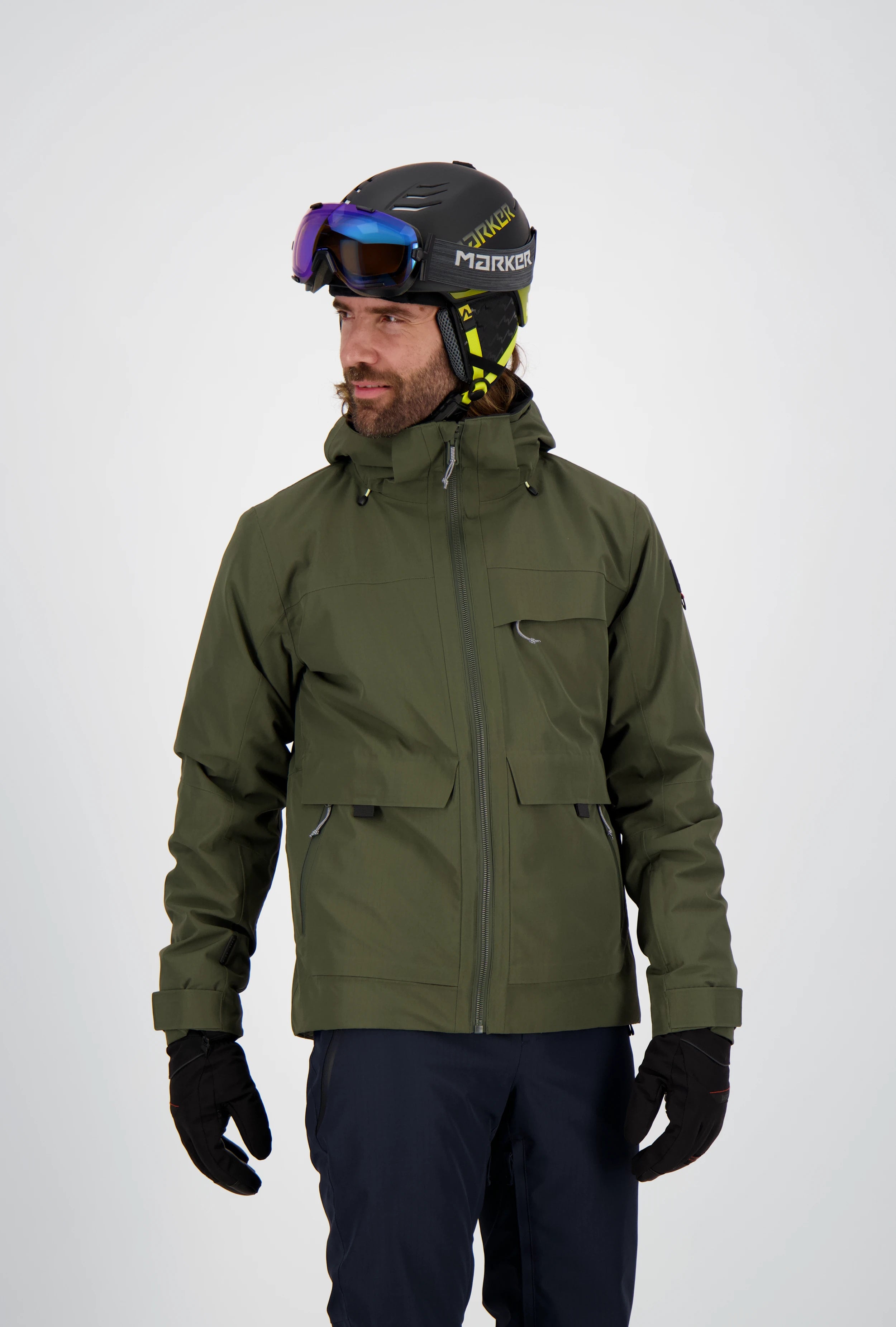 Mann trägt eine olivgrüne Belowzero Herren-Skijacke mit Kapuze und Taschen, dunkle Skihose, schwarze Handschuhe sowie einen Skihelm mit Skibrille.