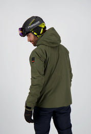Rückansicht eines Mannes in einer olivgrünen Belowzero Skijacke mit Kapuze und Ärmel-Patch, dazu eine dunkle Skihose und Skihelm mit Brille.