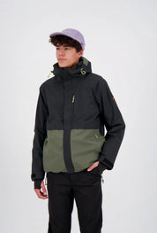 Junger Mann trägt eine zweifarbige Belowzero Outdoor-Skijacke in Schwarz und Olivgrün mit Kapuze, integrierten Handgamaschen und verstellbaren Bündchen, kombiniert mit einer schwarzen Funktionshose und einer hellvioletten Cap.