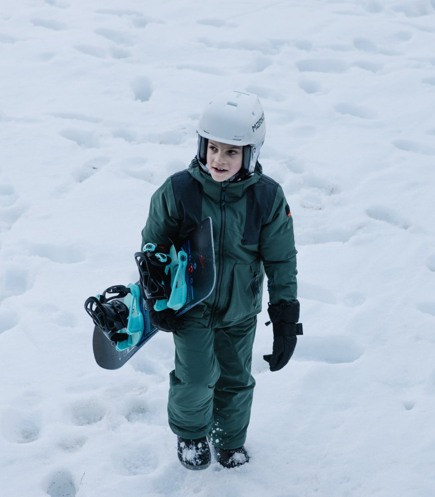Ein Junge in Belowzero Bekleidung sthet im Schnee mit einem Snowboard
