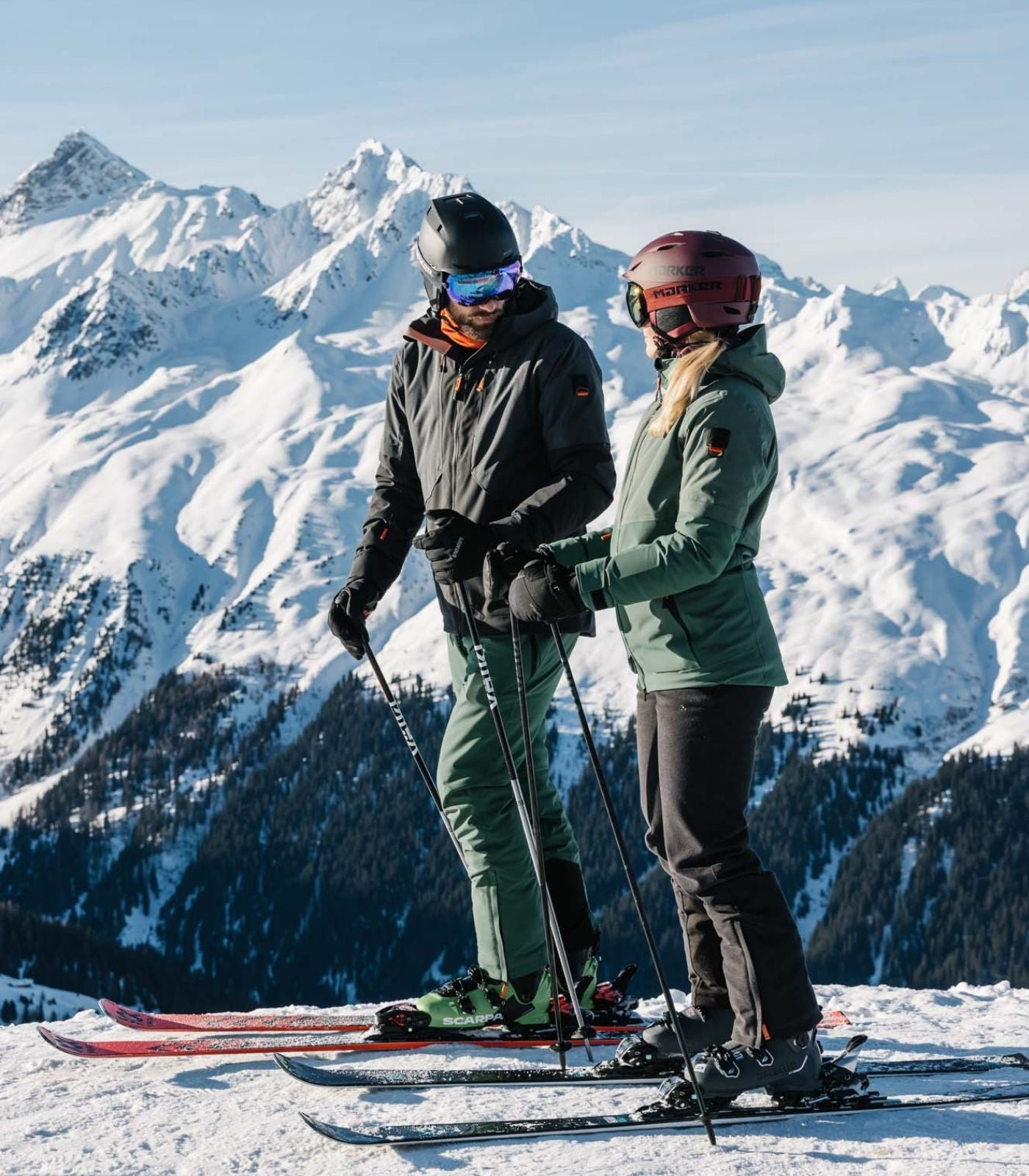 In Mann und eine Frau in kompleter Skiausrüstung stehen auf dem Berg. Im Hintergrund wunderschöne Winterlandschaft.