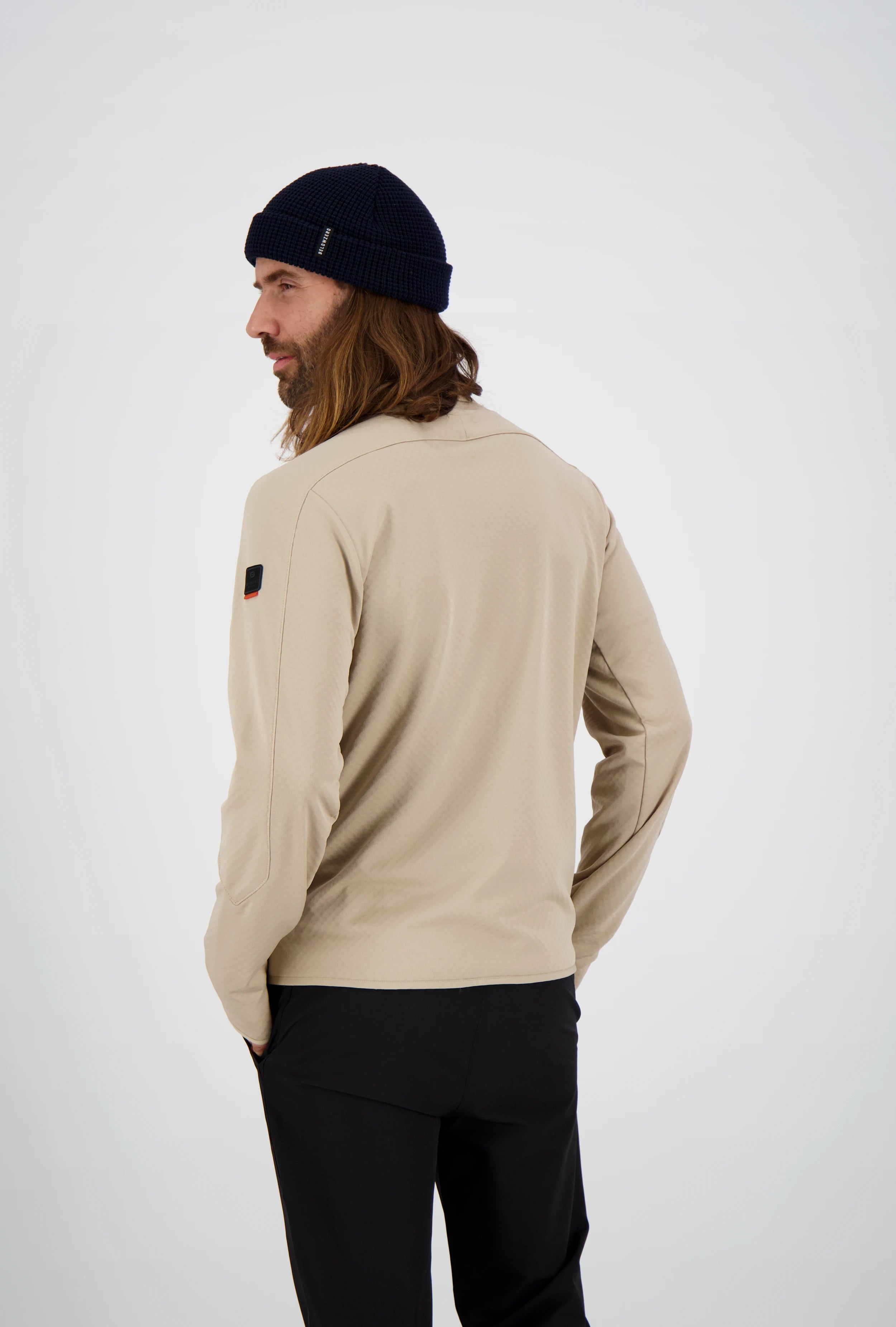 Rückenansicht eines Mannes mit langen Haaren und dunkelblauer Beanie-Mütze in einer beigefarbenen Belowzero Herren Fleecejacke mit Ärmel-Patch und schwarzer Hose.