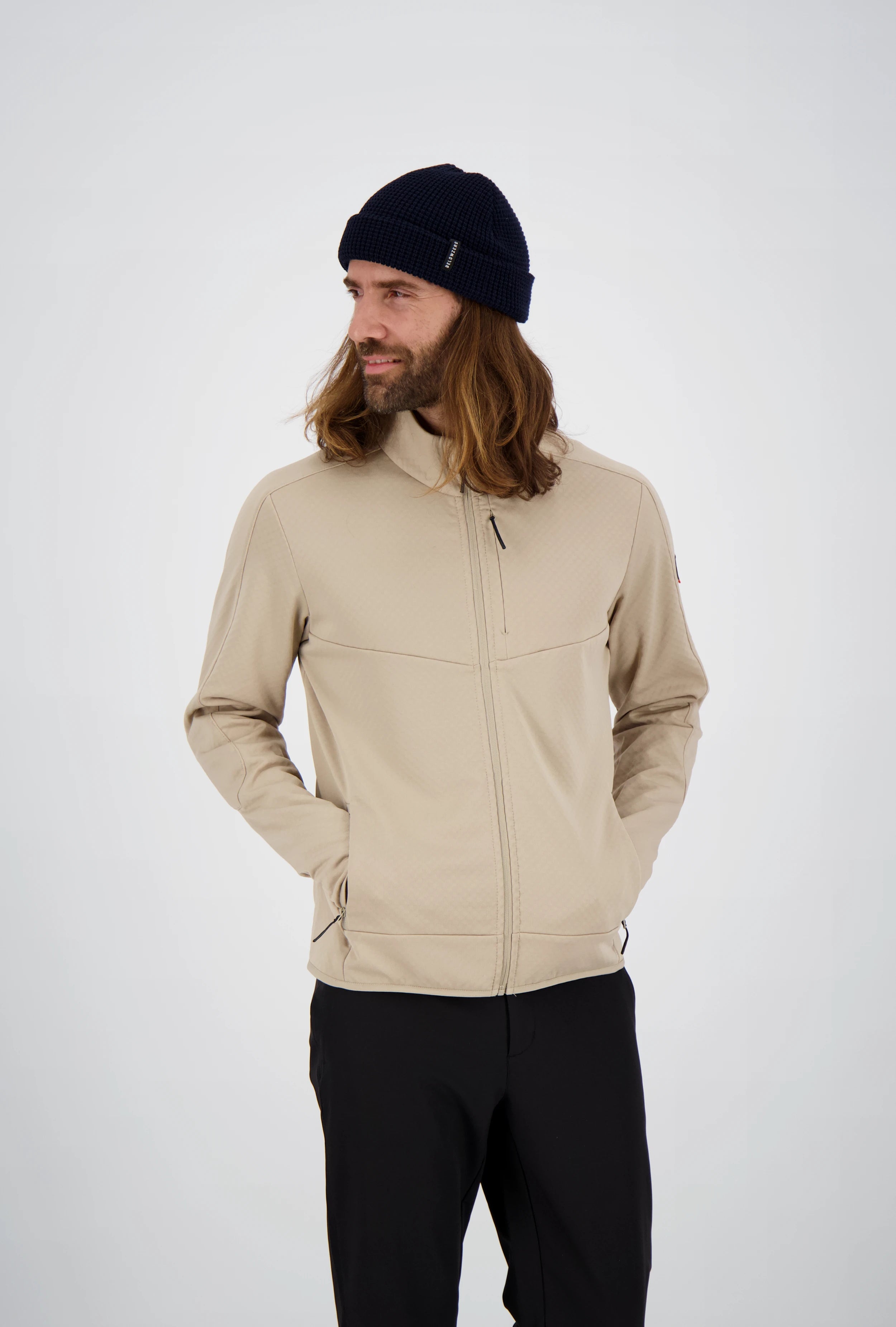 Frontansicht eines Mannes mit langen Haaren und dunkelblauer Beanie-Mütze in einer beigefarbenen Belowzero Herren Fleecejacke Midlayer mit Brusttasche und schwarzer Hose.
