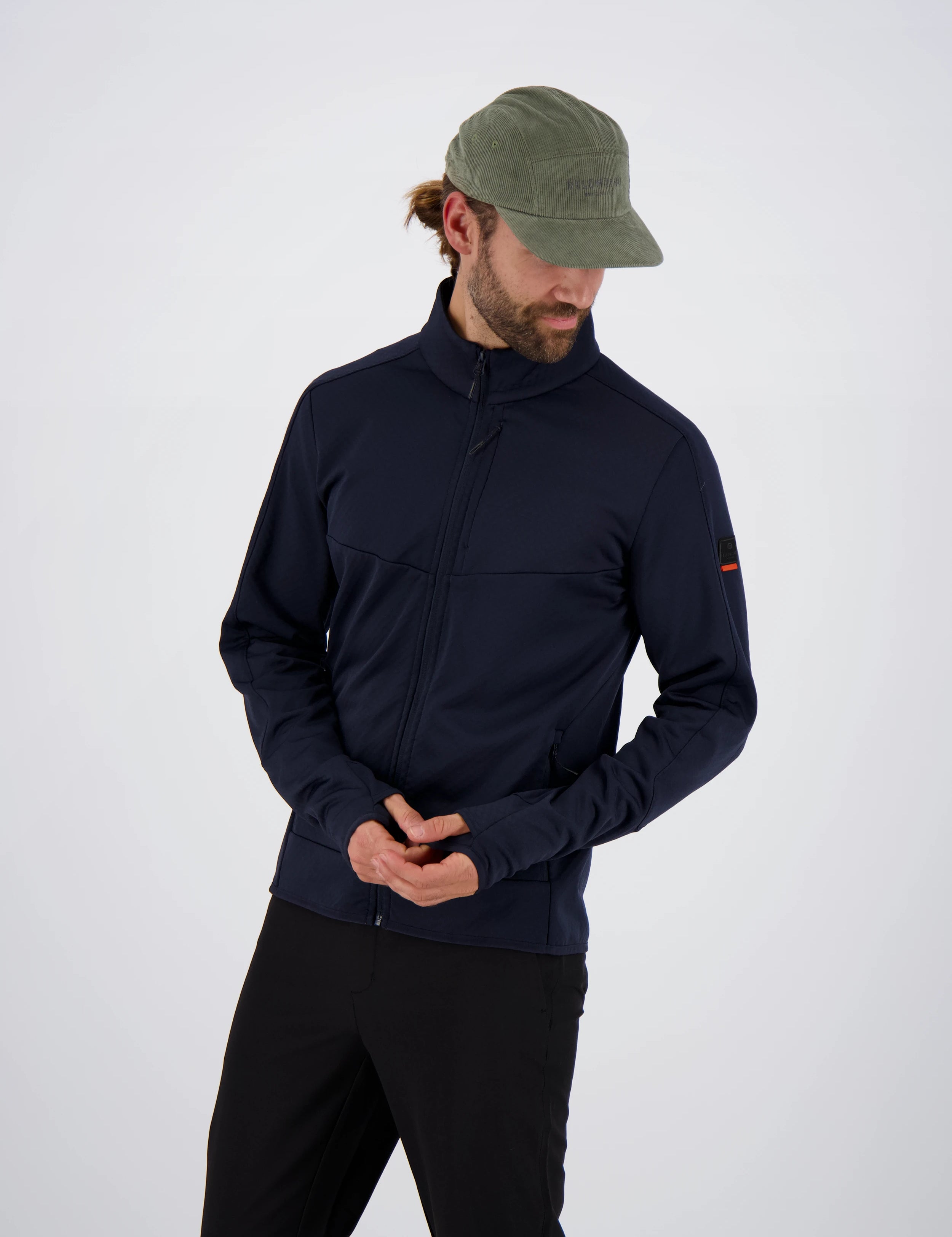 Frontansicht eines Mannes mit olivgrüner Cap in einer dunkelblauen Belowzero Herren Fleecejacke  Midlayer mit Daumenschlaufen und schwarzer Hose.