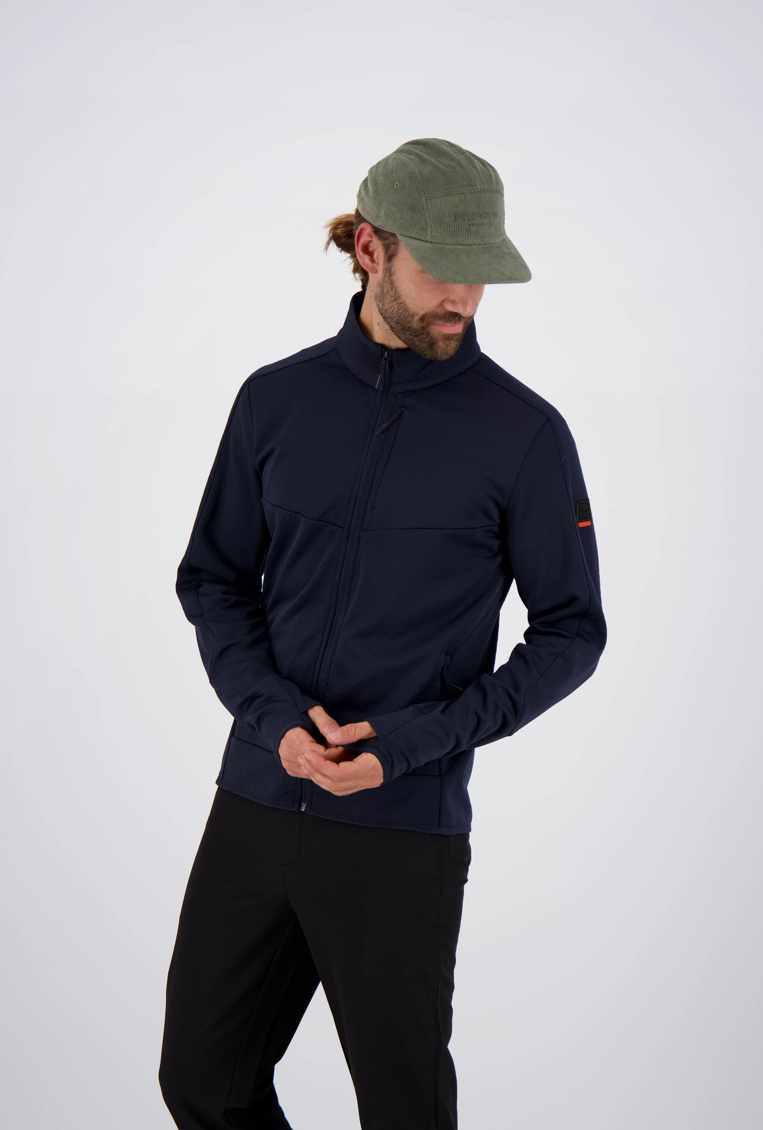Frontansicht eines Mannes mit olivgrüner Cap in einer dunkelblauen Belowzero Herren Fleecejacke  Midlayer mit Daumenschlaufen und schwarzer Hose.