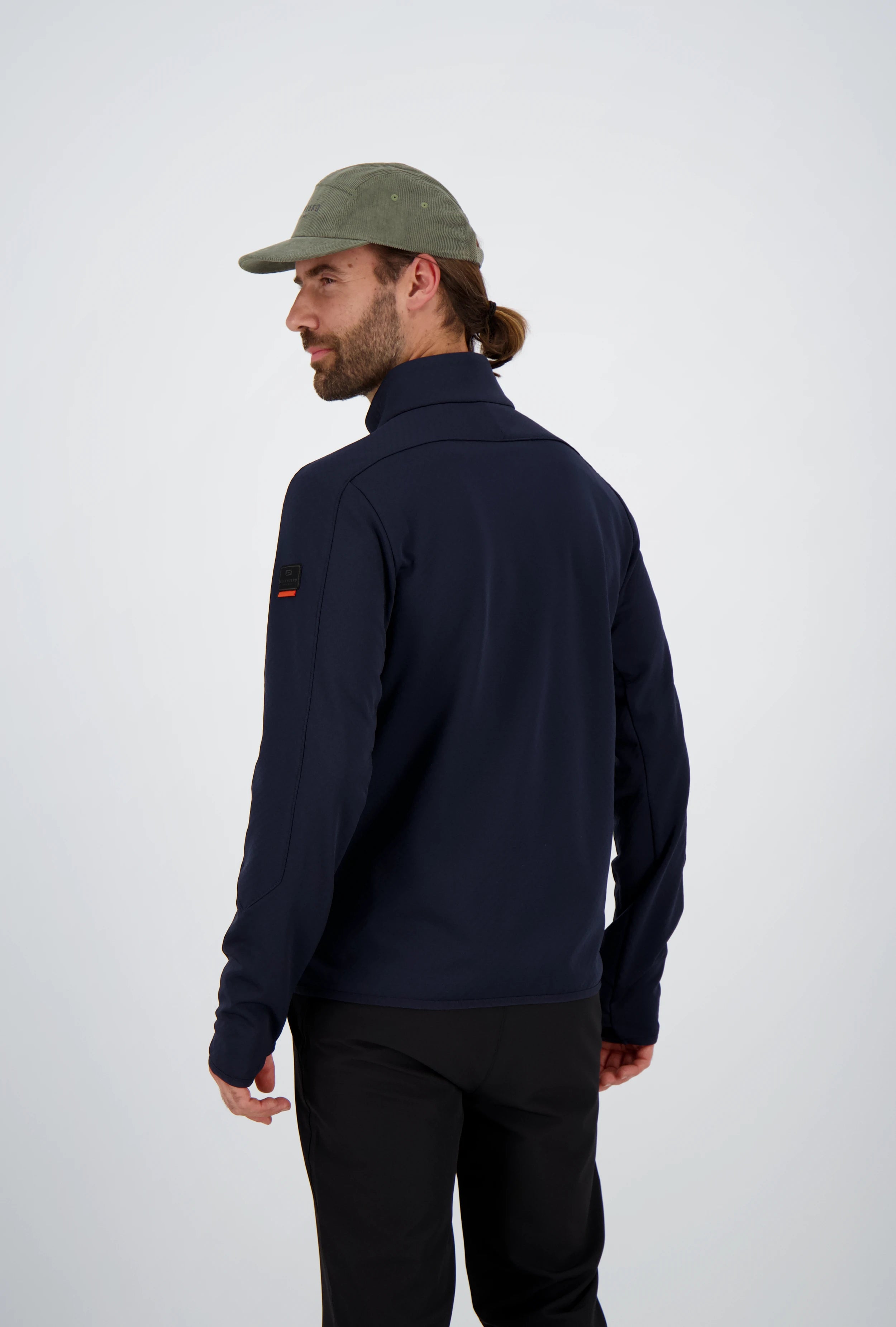 Rückenansicht eines Mannes mit gebundenen Haaren und olivgrüner Cap in einer dunkelblauen Belowzero Herren Fleecejacke Midlayer mit Ärmel-Patch und schwarzer Hose.