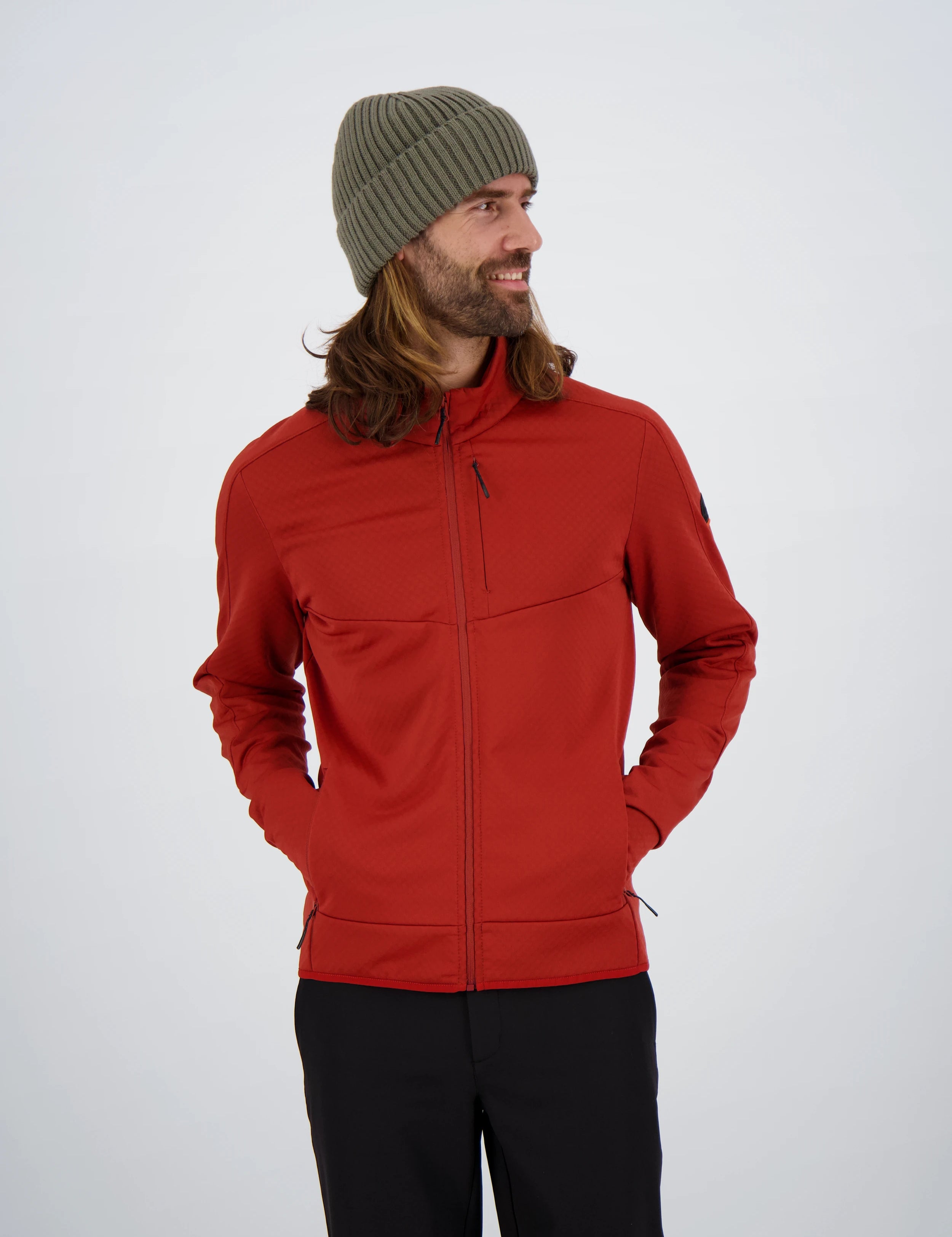 Frontansicht eines Mannes mit langen Haaren und olivgrüner Beanie-Mütze in einer roten Belowzero Herren Fleecejacke Midlayer mit Brusttasche und schwarzer Hose