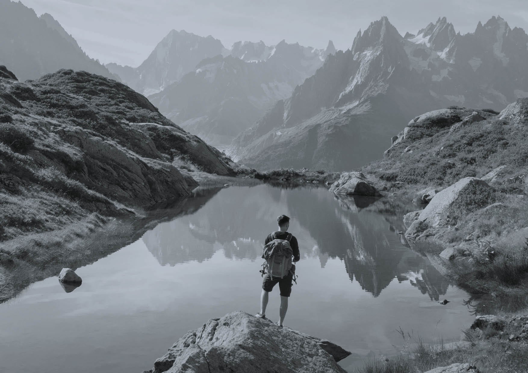 Ein Herr steht mit Wanderausrüstung an einem Bergsee und geniesst die Natur