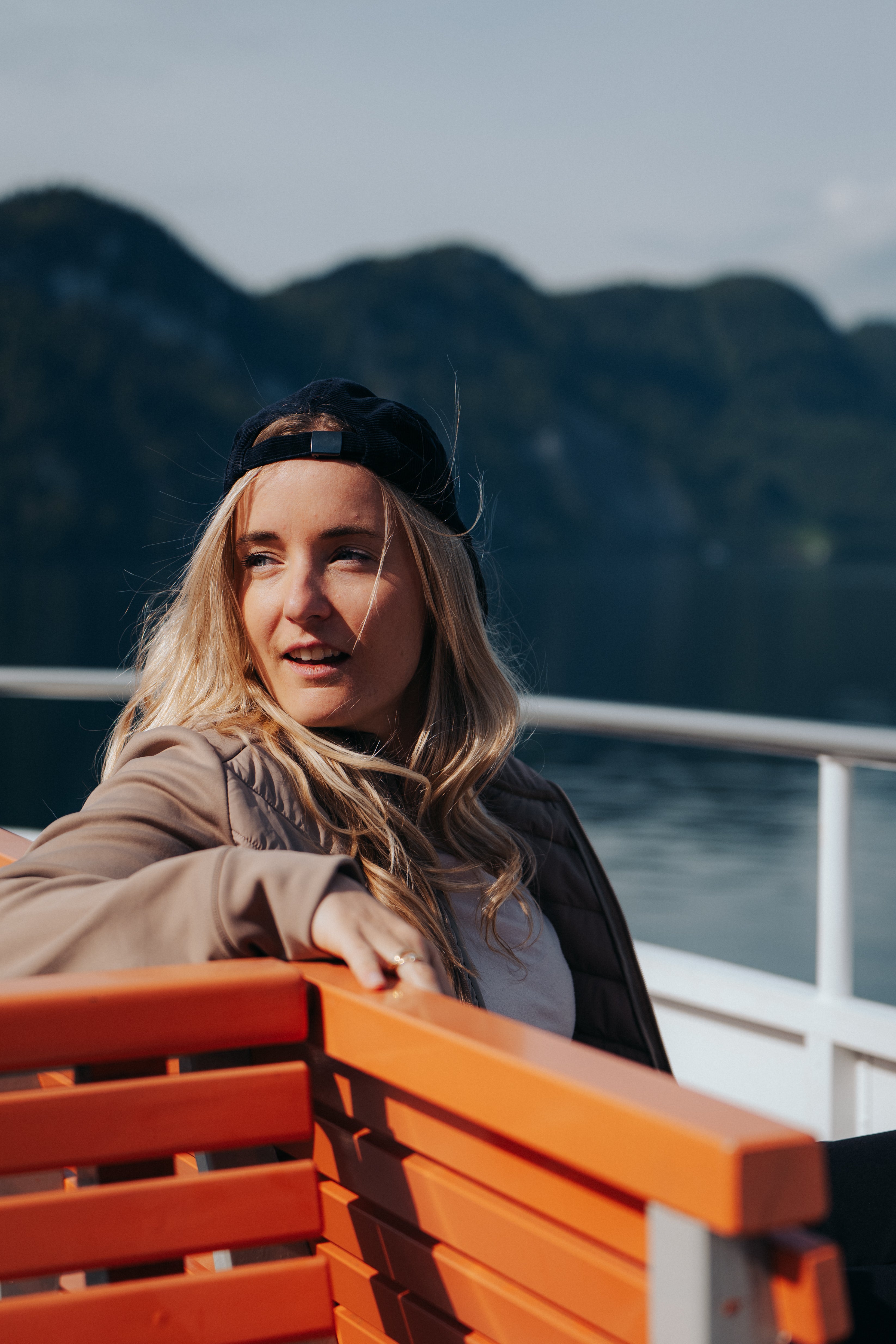 Frau in Belowzero Hybrid Jacke sitzt auf einem Boot vor Bergkulisse am Vierwaldstättersee