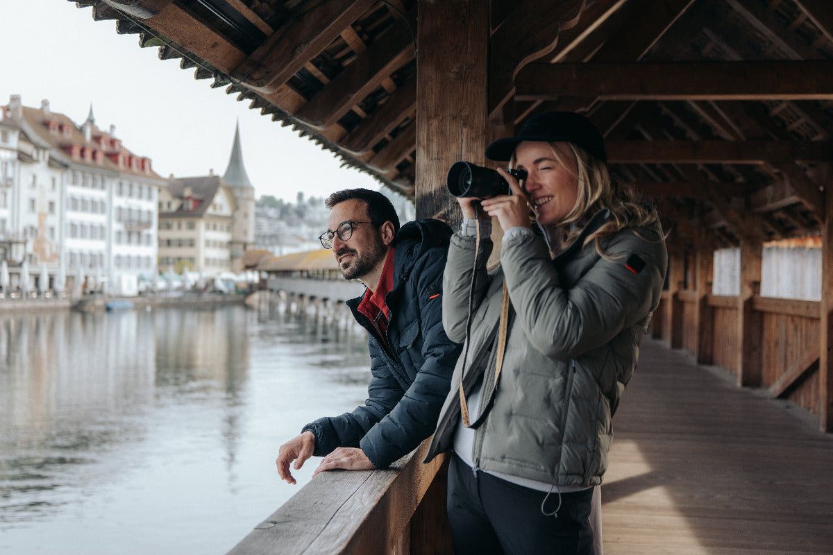 Mann und Frau in Belowzero Funktionsjacken auf der Kapellbrücke in Luzern, Frau fotografiert die Altstadt