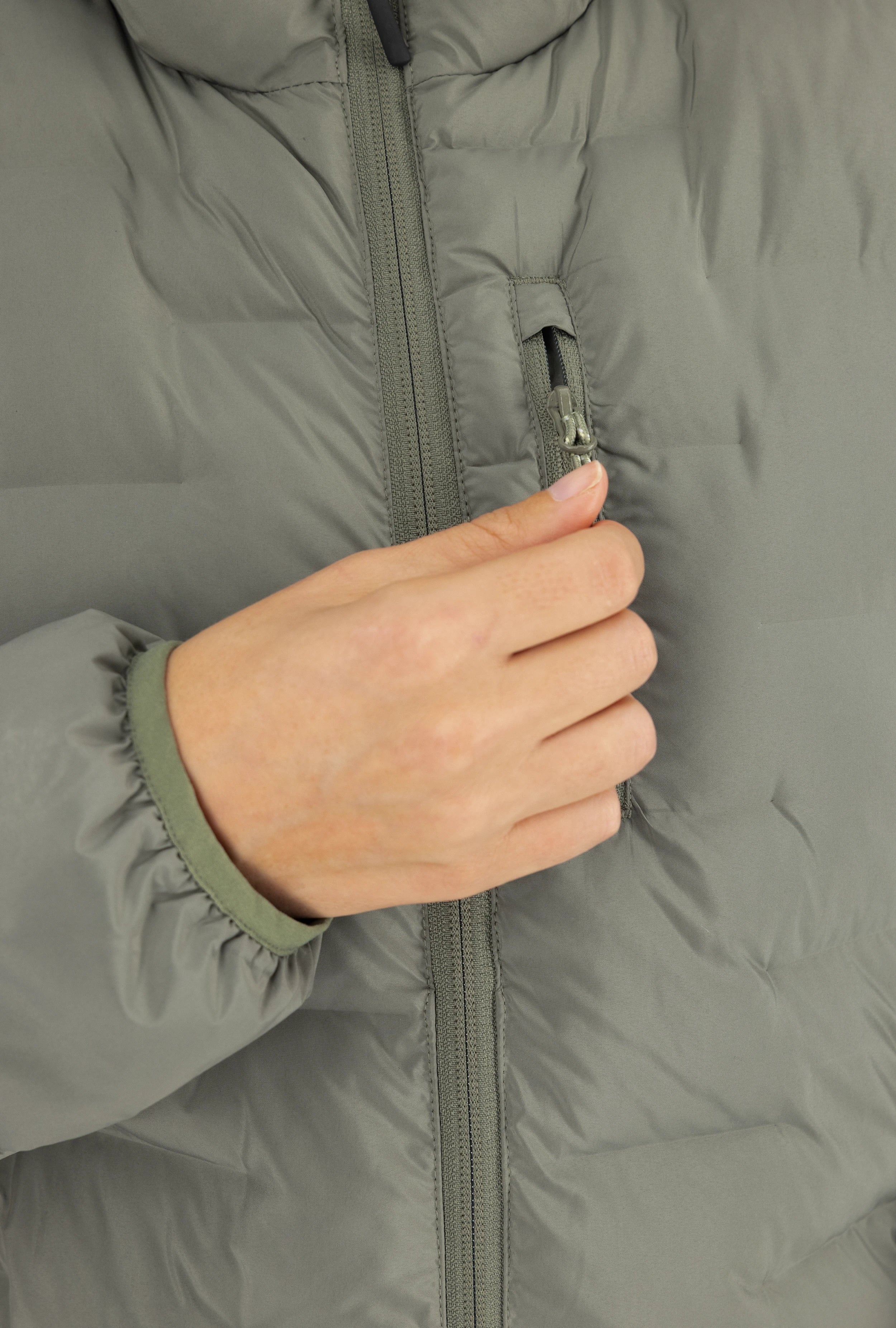 Nahaufnahme einer olivgrünen Belowzero Steppjacke mit Fokus auf die praktische Brusttasche mit Reissverschluss, elastischem Bündchen und robustem Hauptreissverschluss.